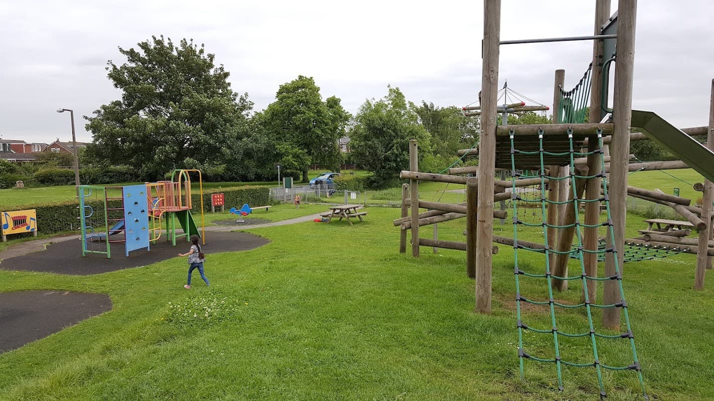 Colorful playground equipment with climbing structures, slides, and grassy areas; trees in the background.
