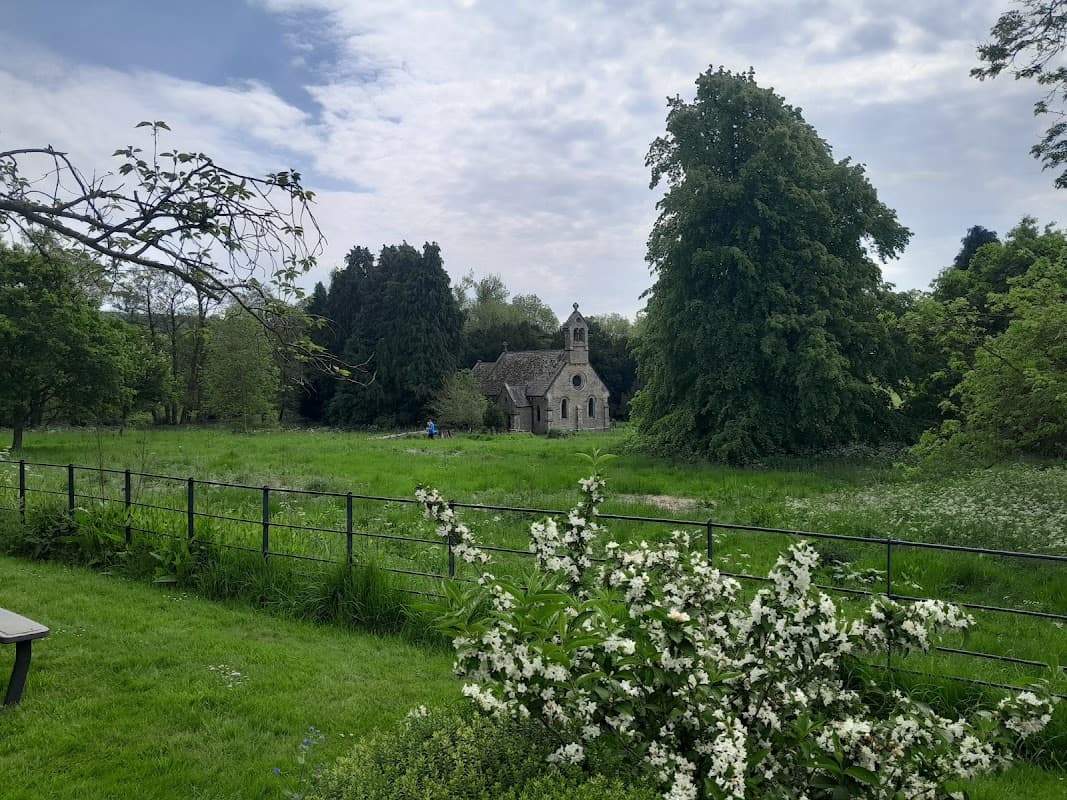 Historic stone church nestled among lush greenery and trees, surrounded by a meadow and blooming white flowers.