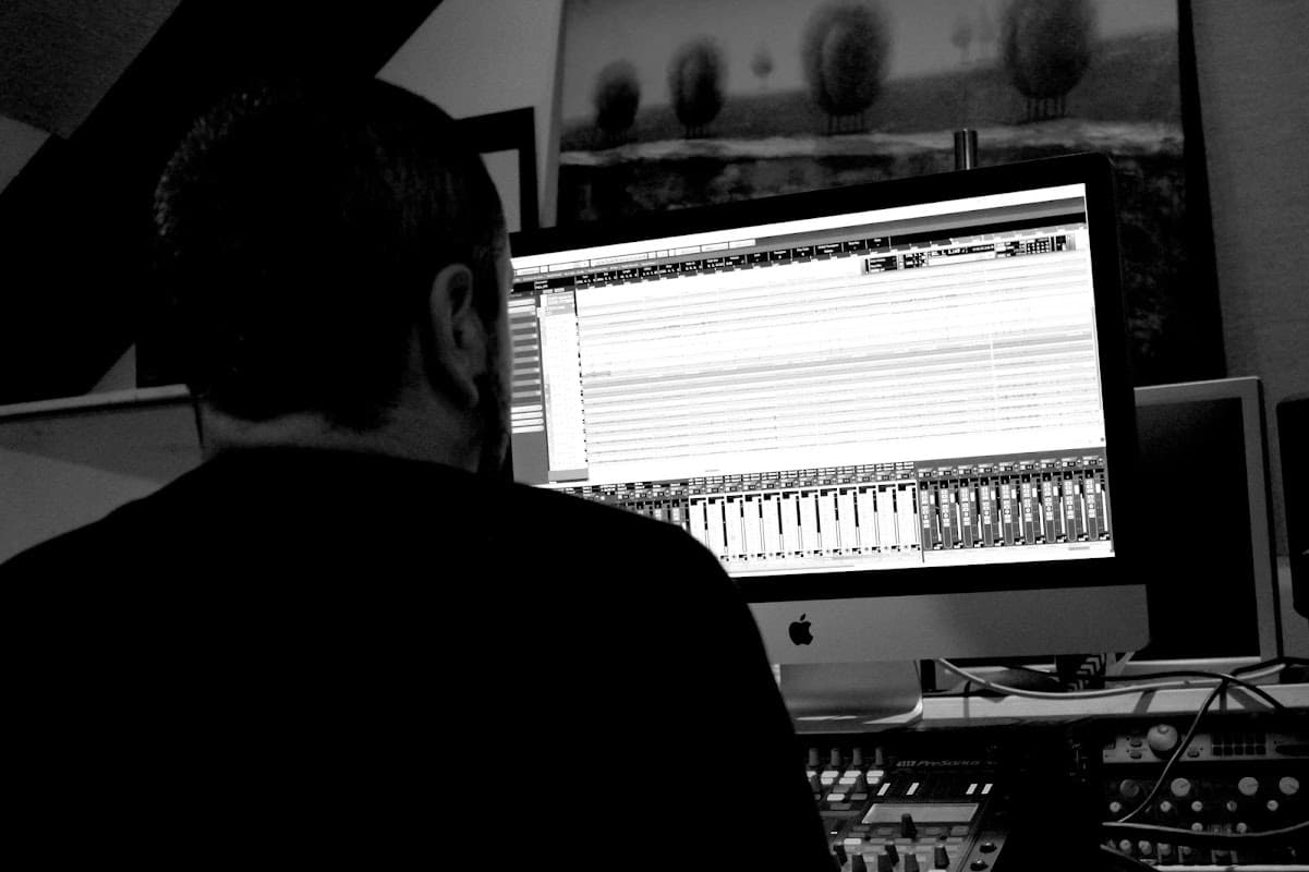 A person working on a music production setup with a large computer screen displaying audio tracks.