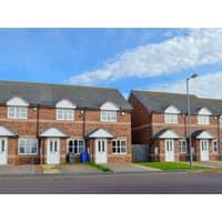Red-brick semi-detached cottages with white doors, gabled roofs, and small front gardens under a blue sky.