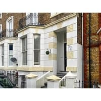 Victorian-style townhouse with white and yellow brick facade, black railings, and arched doorway, by cottages.com.
