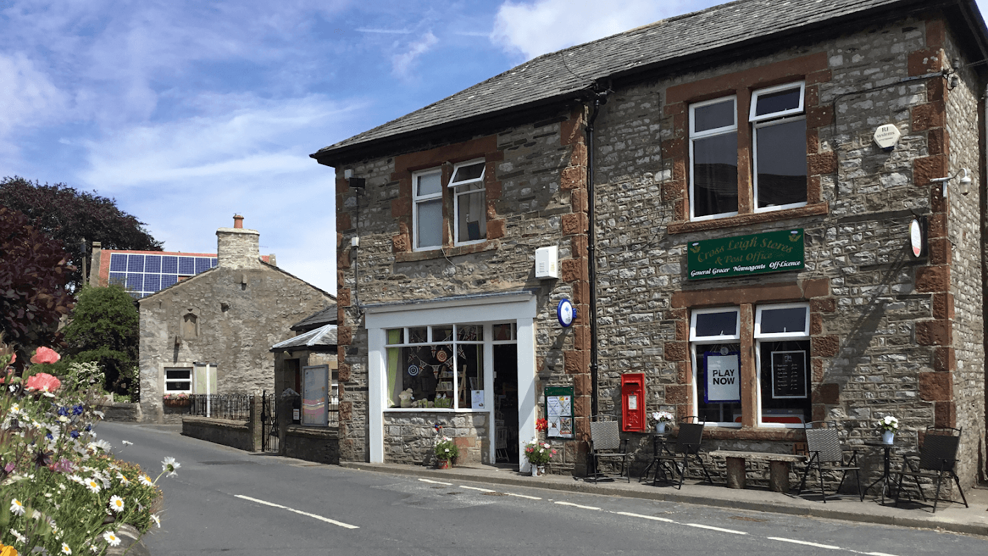 Stone building with a green sign, flower beds, and a red post box, located on a quiet street in Austwick, Yorkshire.